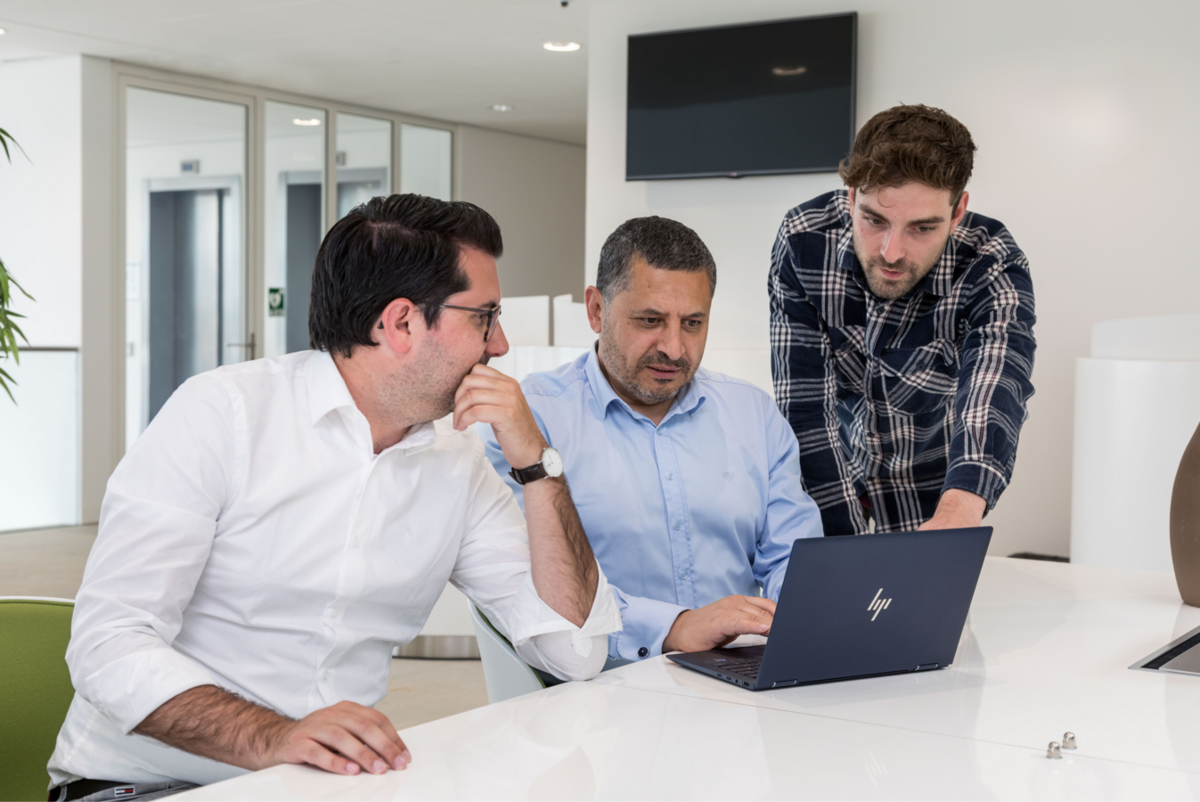 3 men are looking at 1 laptop